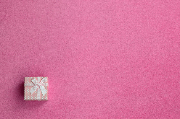 Una pequeña caja de regalo en rosa con un pequeño lazo se encuentra sobre una manta de suave y peludo tejido de lana rosa claro. Embalaje para un regalo a su novia encantadora
 - Foto, imagen