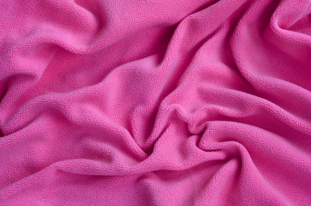 Одеяло из пушистой розовой шерстяной ткани. Фон светло-розовый мягкий плюшевый материал с большим количеством рельефных складок
 - Фото, изображение