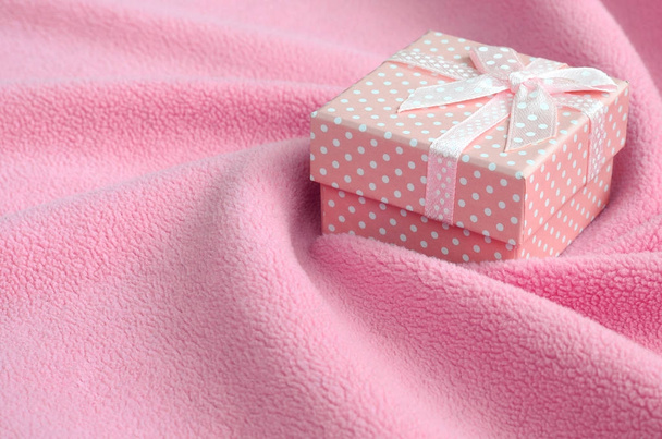 Malý dárek box v růžové barvě s malým lukem leží na deka měkká a chlupaté světle růžové nylonové tkaniny se spoustou úlevu záhyby. Balení jako dárek pro své krásné přítelkyně - Fotografie, Obrázek