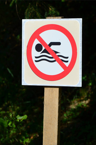 Eine Säule mit einem Schild, das auf ein Badeverbot hinweist. das Schild zeigt eine durchgestrichene schwimmende Person - Foto, Bild