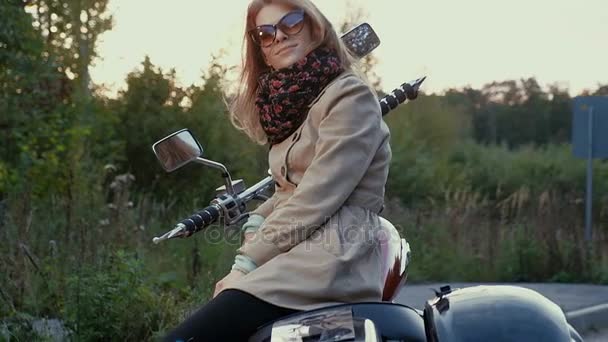 Young girl with brown hair sits on a motorbike near a road. - Video, Çekim