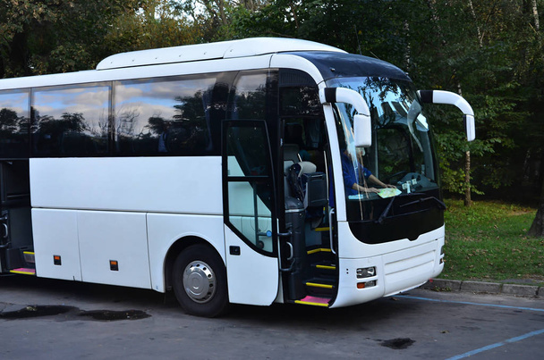 Белый туристический автобус для экскурсий. Автобус припаркован на парковке рядом с парком
 - Фото, изображение
