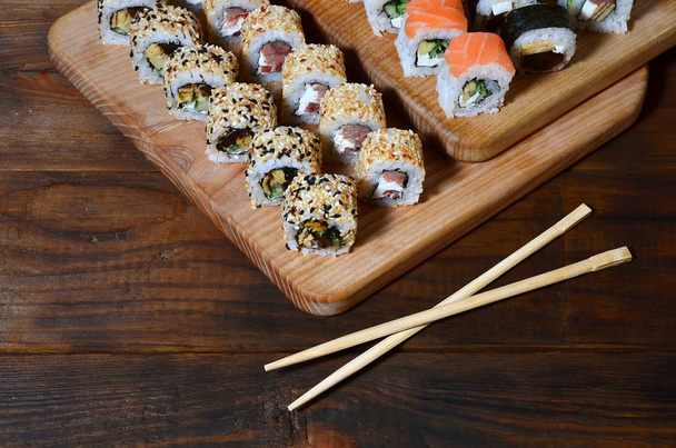 A detailed shot of a set of Japanese sushi rolls and a device for their use (chopsticks), which are located on a wooden cutting board on a table in the kitchen of a sushi bar - Photo, Image