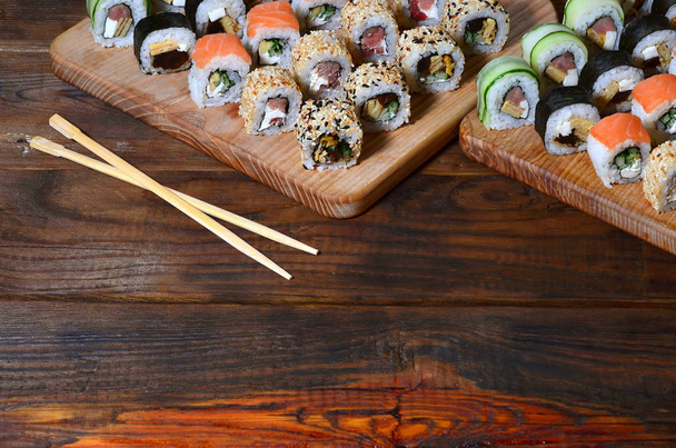 Een gedetailleerde shot van een aantal Japanse sushi rollen en een apparaat voor het gebruik ervan (stokjes), die zich op een houten snijplank op een tafel in de keuken van een sushibar bevinden - Foto, afbeelding