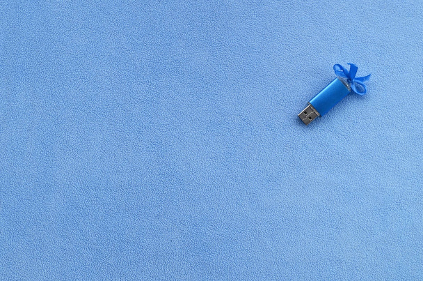 Ragyogó kék usb flash memória kártya-val egy kék íj fekszik egy takaró puha és Szőrős világos kék gyapjú szövet. Klasszikus női ajándék design memóriakártya - Fotó, kép