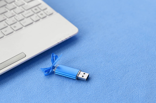 Brillante scheda di memoria flash USB blu con un fiocco blu si trova su una coperta di tessuto morbido e peloso in pile blu chiaro accanto a un computer portatile bianco. Design regalo femminile classico per una scheda di memoria
 - Foto, immagini