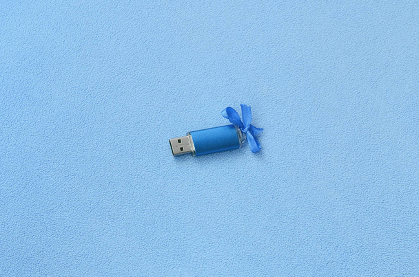 Ragyogó kék usb flash memória kártya-val egy kék íj fekszik egy takaró puha és Szőrős világos kék gyapjú szövet. Klasszikus női ajándék design memóriakártya - Fotó, kép