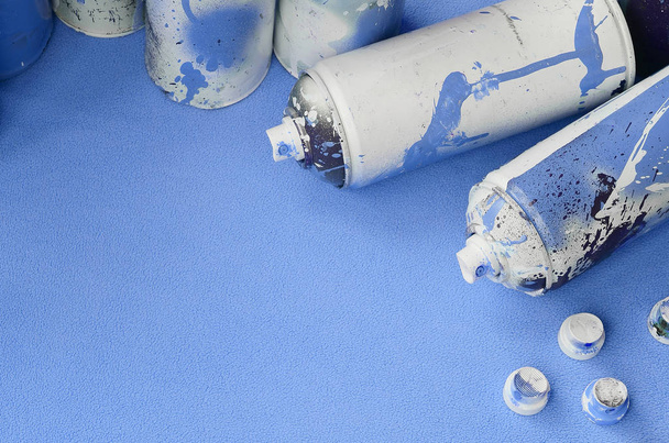 einige gebrauchte blaue Spraydosen und Düsen mit Farbtropfen liegen auf einer Decke aus weichem und pelzigem hellblauem Fleece-Stoff. klassische weibliche Designfarbe. Konzept für Graffiti-Rowdytum - Foto, Bild