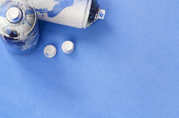 Některé použité modré aerosolové spreje a trysky s barva nekape leží na dece měkké a chlupaté světle modrá fleece tkaniny. Klasický ženský design barva. Graffiti chuligánství koncept - Fotografie, Obrázek
