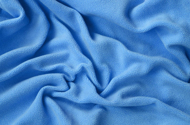 Одеяло из шерстяной синей шерстяной ткани. Фон светло-голубой мягкий плюшевый флисовый материал с большим количеством рельефных складок
 - Фото, изображение