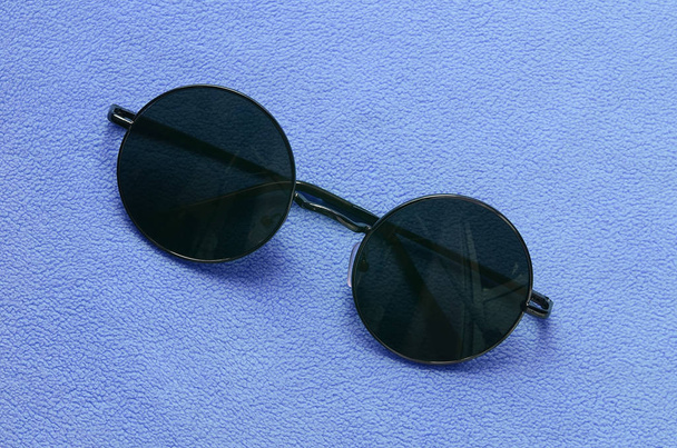 Elegantes gafas de sol negras con gafas redondas se encuentra en una manta hecha de suave y esponjosa tela de lana azul claro. Imagen de fondo de moda en colores femeninos
 - Foto, Imagen