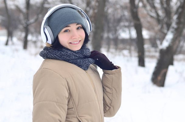 Portrait of pretty attractive caucasian pierced girl hipster winter park. She is listening to music on headphones. Youth street fashion. Winter fun. - Photo, Image