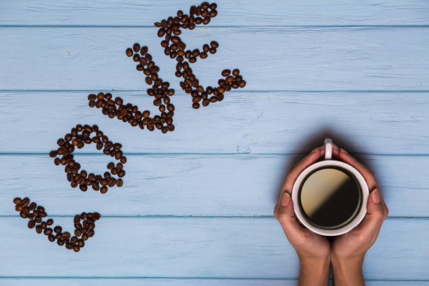 Woman's hands hold cap of coffee on a blue wooden table, view above. Love text from coffee beans on a blue wooden table - Photo, Image