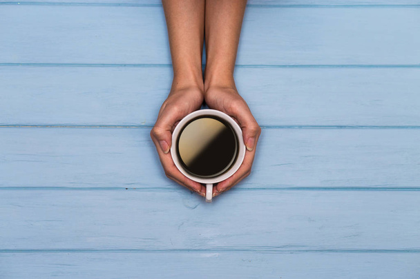 Woman's hands hold cap of coffee on a blue wooden table, view above - Photo, Image