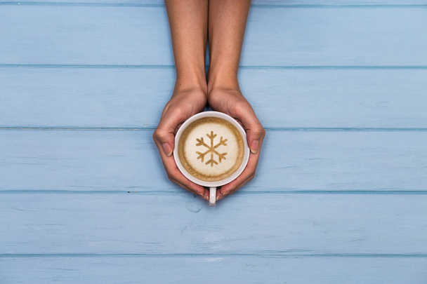 Vrouw handen houd GLB koffie met sneeuwvlok sieraad op een blauwe houten tafel, bekijken boven.  - Foto, afbeelding