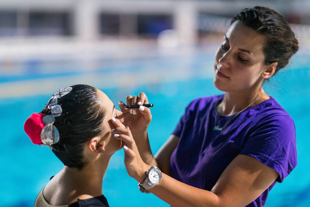 trainer Applaying make up prima della competizione sulla competizione di nuoto sincronizzato
 - Foto, immagini