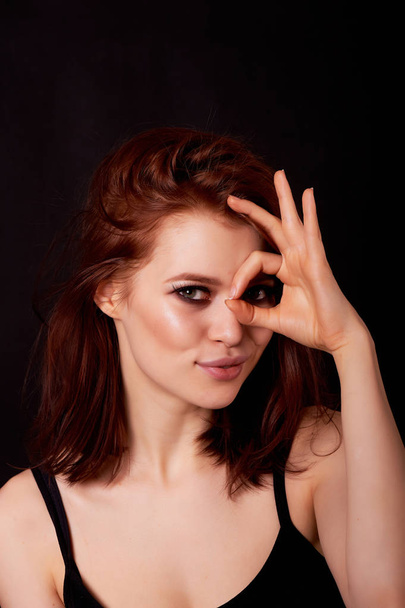 Girl in Studio on dark background. Red hair, great figure. Shows a positive gesture that everything is cool.Life is beautiful and positive - Foto, afbeelding