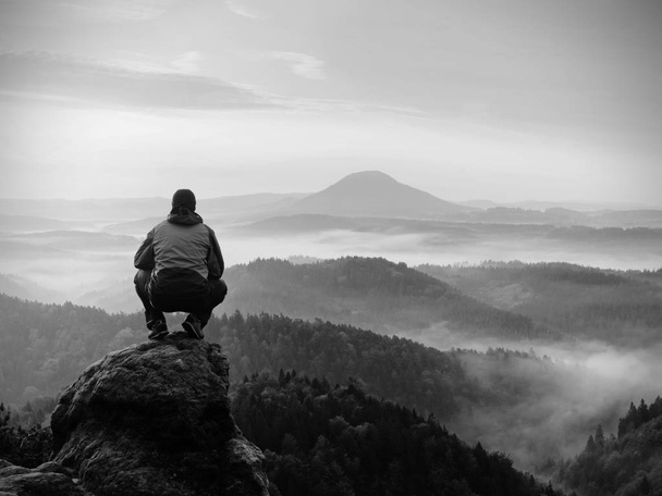 L'homme reste sur le pic rocheux au lever du jour et veille sur le paysage brumeux
. - Photo, image