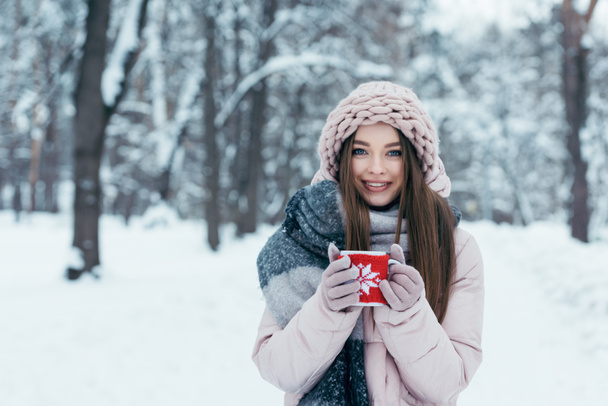 gyönyörű fiatal nő portréja, csésze forró kávé társaságában kezét havas park - Fotó, kép