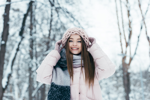 portrait of smiling woman in winter clothing looking at camera in snowy park - Foto, afbeelding