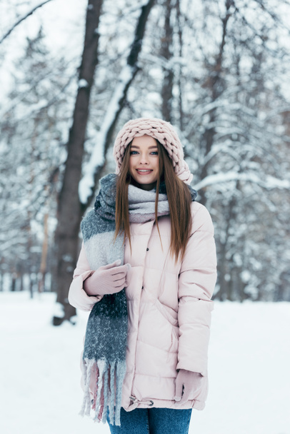 portrét usmívající se žena v zimním oblečení při pohledu na fotoaparát v zasněženém parku - Fotografie, Obrázek