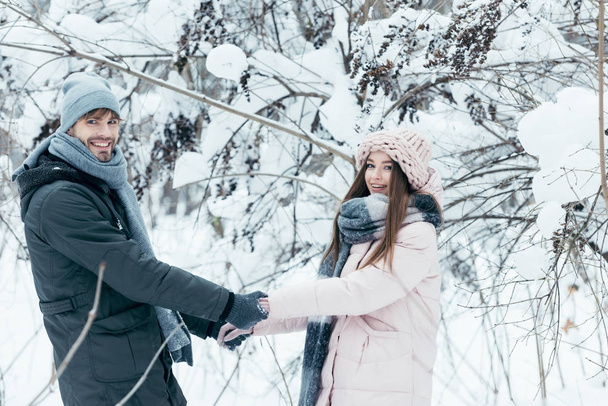 hymyilevä pari kädestä ja katsot kameraa lumisessa metsässä
 - Valokuva, kuva