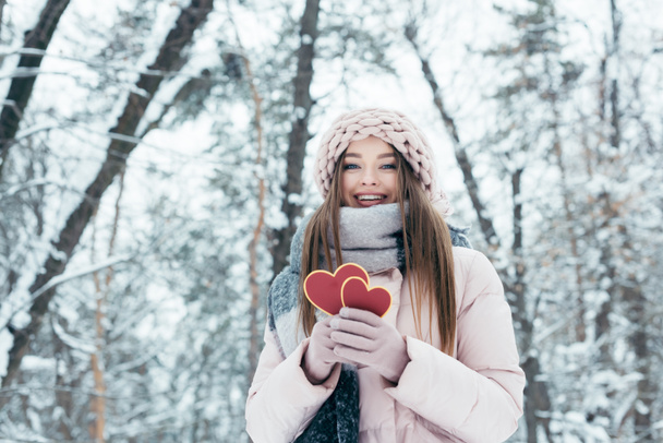 portrait of beautiful young woman with hearts in hands looking at camera in snowy park - Photo, Image