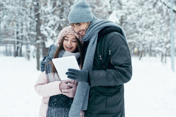 portrait of young happy couple with tablet in snowy park - Zdjęcie, obraz