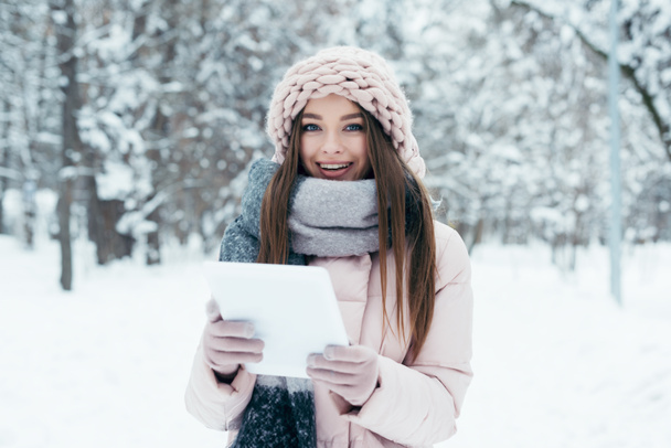 portrait of smiling young woman with tablet in winter park - Photo, Image