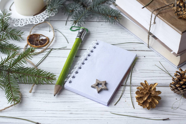 A festive winter mock up photo with a fir twigs, an opened note book, an old book, a pencil, cones, a candle and decation elements - 写真・画像
