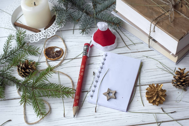 A festive winter mock up photo with a fir twigs, an opened note book, an old book, a pencil, cones, a candle and decation elements - Photo, Image