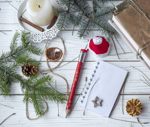 A festive winter mock up photo with a fir twigs, an opened note book, an old book, a pencil, cones, a candle and decation elements - Foto, imagen