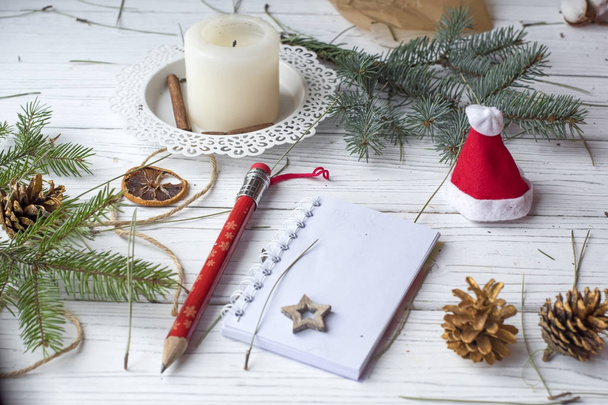 A festive winter mock up photo with a fir twigs, an opened note book, an old book, a pencil, cones, a candle and decation elements - Foto, immagini