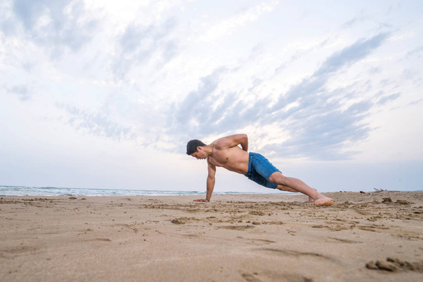 Fitness-Mann macht Liegestütz am Strand. Porträt eines fitten Kerls, der seine Armmuskeln und seinen Körperkern mit Liegestützübungen am Sandstrand trainiert. - Foto, Bild