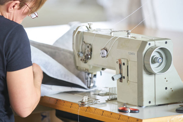 Seamstress or worker in a factory sewing with a industrial sewing machine - Foto, Bild