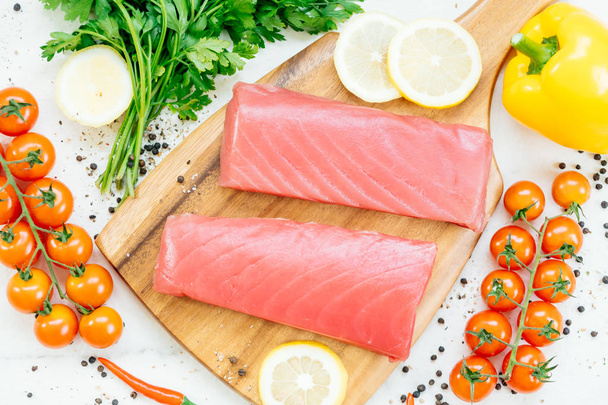 Carne de filé de atum cru em tábua de corte de madeira com vegetal e ingrediente para cozinhar
 - Foto, Imagem