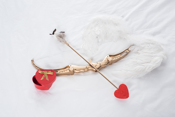 κάτοψη του δώρου, φτερά, τόξο και τα βέλη σε λευκό κρεβάτι - Φωτογραφία, εικόνα