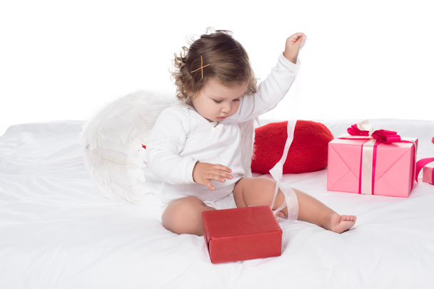 petit ange assis sur le lit avec des boîtes-cadeaux, isolé sur blanc
 - Photo, image
