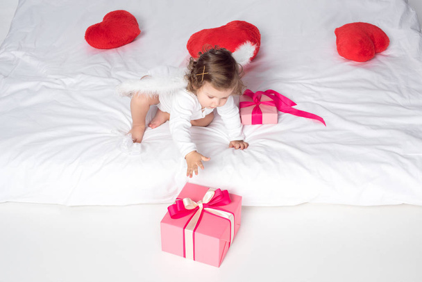 małego aniołka ze skrzydłami na łóżku z serca i prezenty - Zdjęcie, obraz