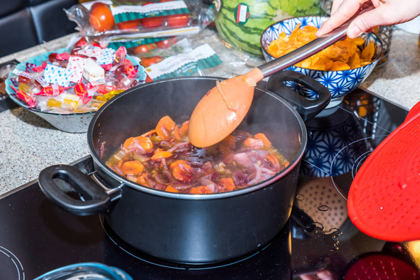 現代の電気コンロの上に鍋鍋で揚げる新鮮なニンジン玉ねぎキャベツをステアリング女性の手 - 写真・画像