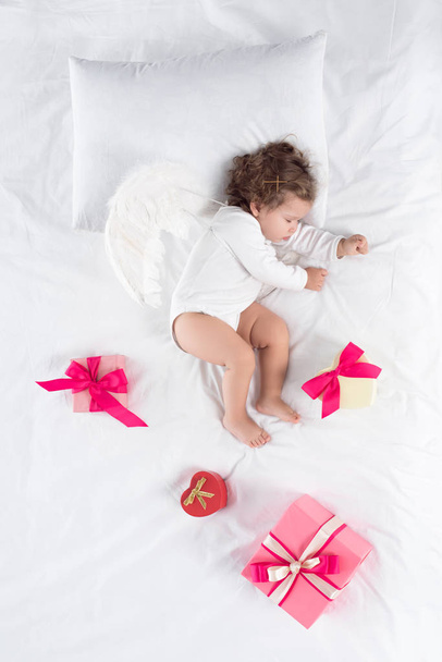 petit chérubin avec des ailes couchées sur le lit avec des cadeaux
 - Photo, image