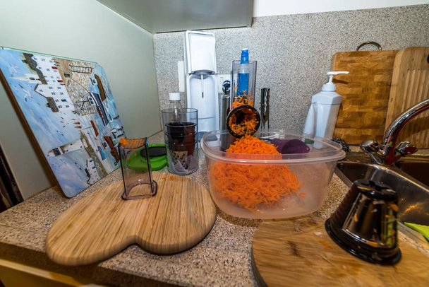 Ψιλοκομμένα καρότα σε πλαστικό δοχείο στο τραπέζι της κουζίνας έτοιμο για μαγείρεμα - Φωτογραφία, εικόνα