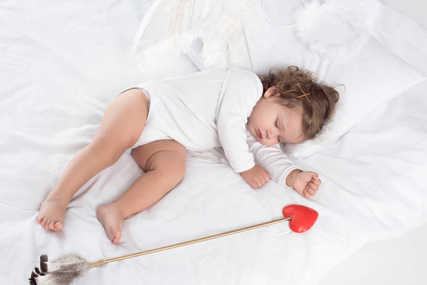 little cupid with wings sleeping on bed with arrow  - Φωτογραφία, εικόνα