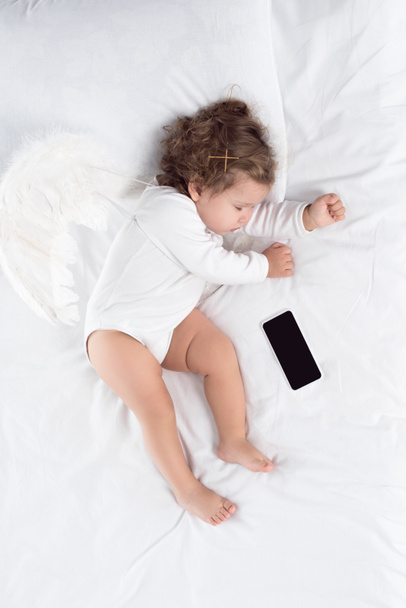 pieni enkeli nukkuu sängyssä älypuhelimen kanssa
 - Valokuva, kuva