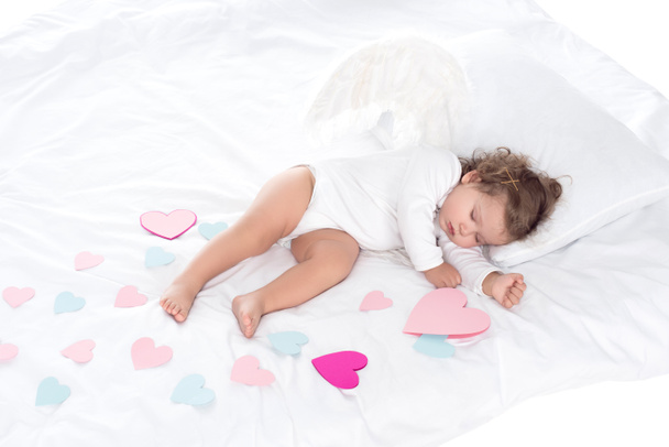 little sleepy cherub with wings lying on bed with hearts  - Foto, Imagem