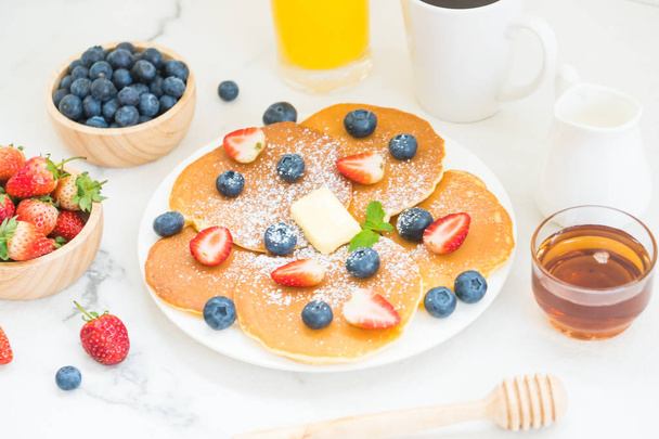 Gezond ontbijt instellen met Pancake bosbessen en aardbeien vruchten, zwarte koffie, melk en jus d'orange op witte stenen tafel achtergrond - Foto, afbeelding