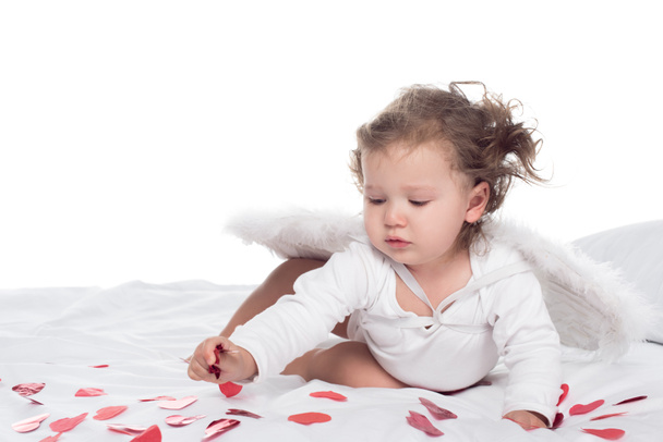 kleine Cupido met vleugels op bed met harten, geïsoleerd op wit - Foto, afbeelding