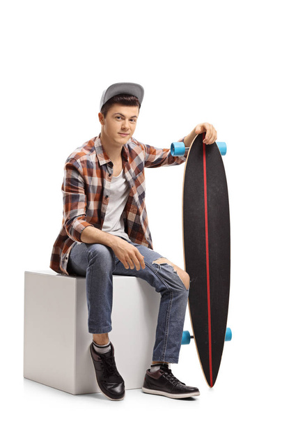 Teenage hipster with a longboard sitting on a cube - Φωτογραφία, εικόνα