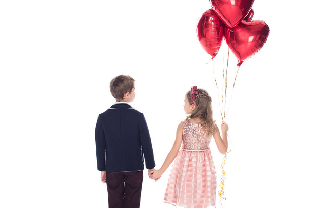 rear view of adorable little kids with heart shaped balloons holding hands isolated on white  - Foto, Bild
