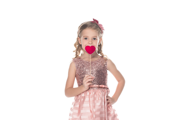 adorable little kid in pink dress holding red heart on stick and looking at camera isolated on white - Photo, Image
